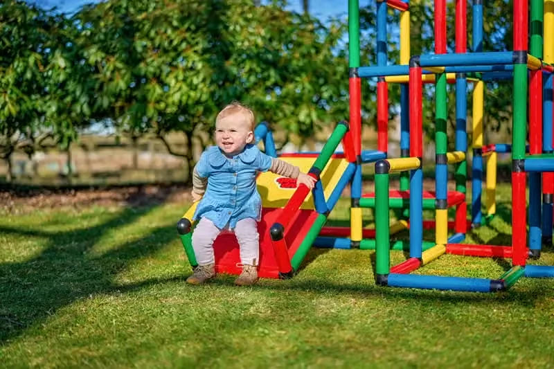 Toddler seated on a small red ramp beside a large QUADRO climbing tower