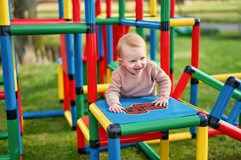 Toddler leaning on a blue QUADRO platform beside the climbing tower