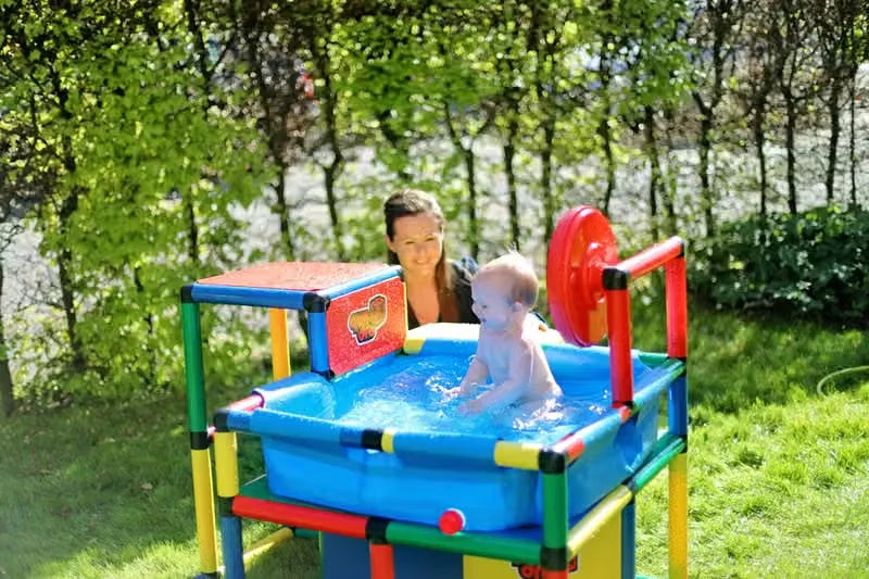 Adult supervising a baby seated in a compact blue QUADRO pool outdoors