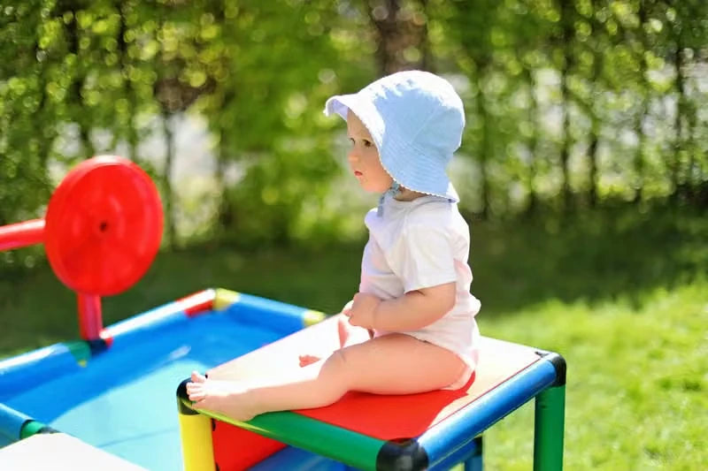 Baby in a sun hat seated on the red platform beside a QUADRO pool