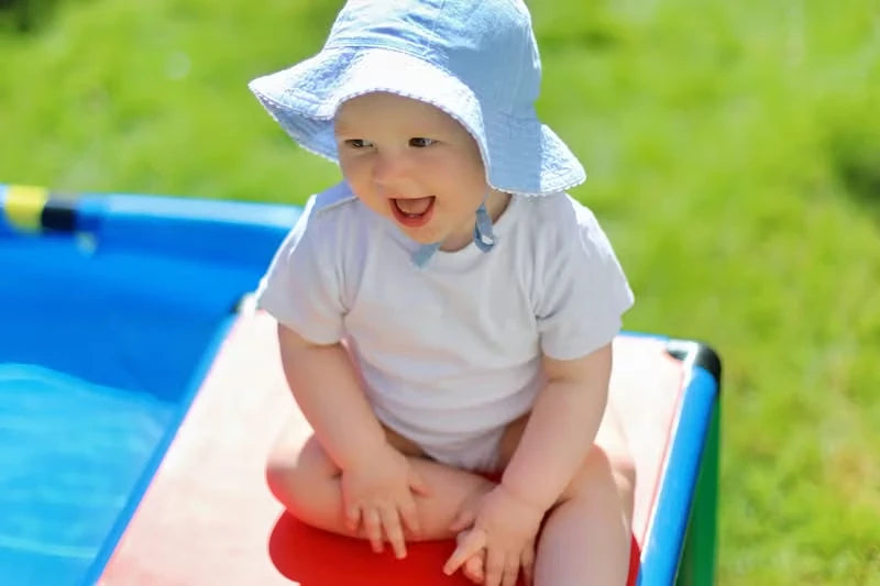 Smiling baby seated on a red QUADRO platform beside a blue pool