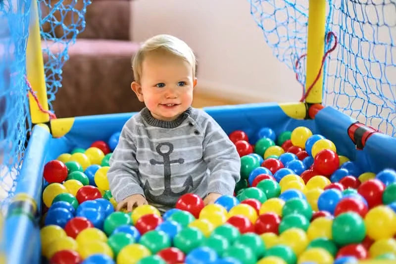 Smiling toddler seated among red, yellow, green and blue play balls