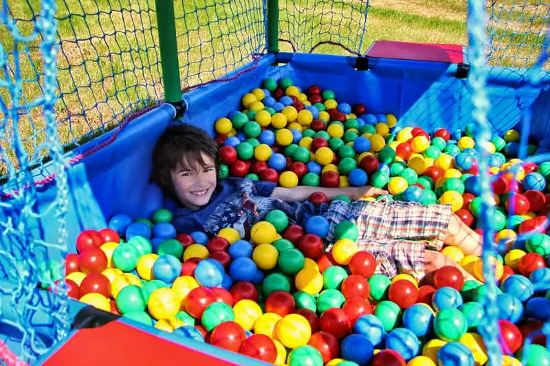 Child lying among colourful balls inside a large netted QUADRO pool